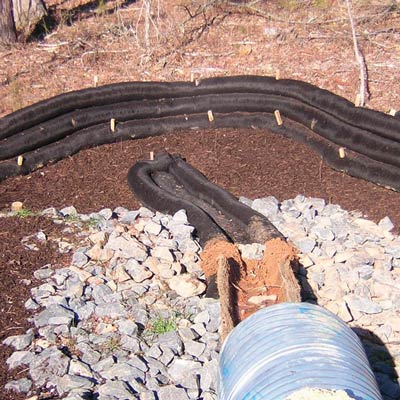 Black filter socks stacked to filter runoff from rock outfall pipe and protect surrounding soil.